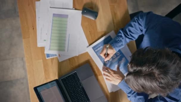 Empresario Sentado en Su Escritorio en la Oficina Utiliza Computadora Portátil, Trabajando con Documentos de Estrategia de la Compañía, Corrección de Gráficos, Dibujo Gráficos y Estadísticas. Vista superior Zoom Fuera de tiro giratorio — Vídeo de stock