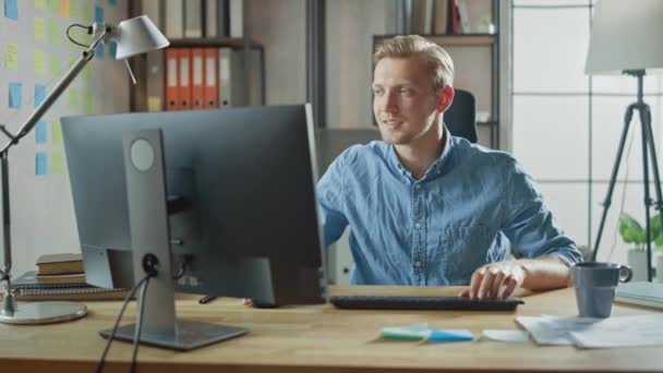 Kreativer Unternehmer sitzt an seinem Schreibtisch und arbeitet am Desktop-Computer im stilvollen Büro. Schöner Kaukasier nutzt Computer. Im Hintergrund stilvolles Büro-Studio mit modernem Minimalismus-Design — Stockvideo