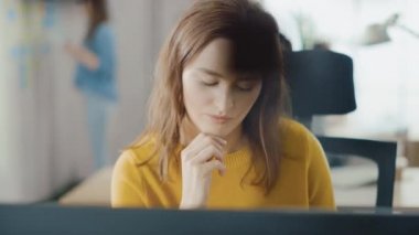 Güzel ve zeki kızıl saçlı kadın uzmanı masasında oturuyor. Masaüstü bilgisayarında çalışıyor. Yetenekli Yaratıcı İnsanlar İçin Ergonomik Mobilyalı Parlak ve Modern Açık Uzay Ofisi