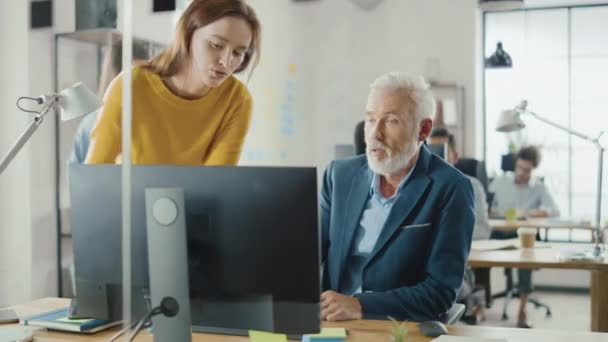 Ingeniero creativo guapo de mediana edad sentado en el escritorio que trabaja en la computadora de escritorio tiene discusión con la gestora de proyectos femenina hermosa. Oficina con Colegas Amistosos Charlando, Encontrar Soluciones — Vídeo de stock