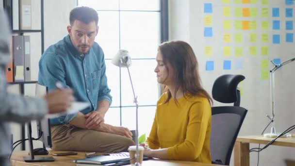 Spécialiste féminine travaille sur ordinateur de bureau, gestionnaire de projet convivial s'assoit sur la table à côté et donne des conseils sur l'optimisation de la gestion de l'expérience client. Bureau moderne avec équipe diversifiée — Video