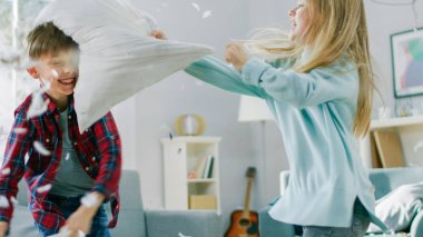 Sevimli Küçük Çocuk ve Tatlı Küçük Kız Güneşli Oturma Odasında Bir Yastık Fight var. Yastıklarla Kavga EtmekLe Eğlenen Kardeşler, Etrafta Uçan Tüyler.