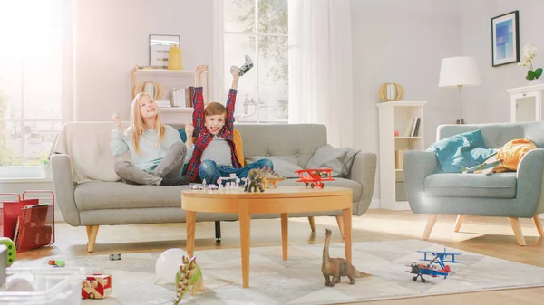 Zu Hause: Smart Boy spielt in Videospielkonsole, Steuerung per Joystick, seine ältere Schwester sitzt in der Nähe auf dem Sofa und feuert ihn an. Sie gewinnen und feiern fröhlich. Glückliche Kinder, die Videospiele spielen. — Stockfoto