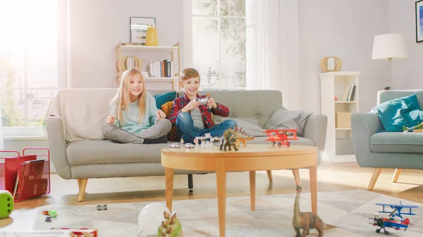 Em casa: Smart Boy Jogando no console de videogame, usando o Joystick Controller, sua irmã mais velha se senta perto do sofá e aplaude ele. Crianças felizes jogando Videogames juntos . — Fotografia de Stock