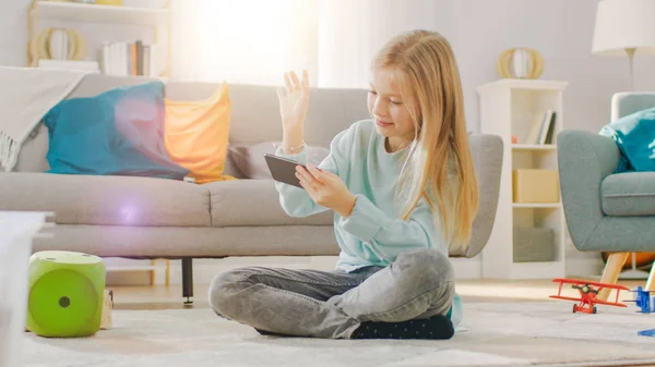 Intelligentes nettes Mädchen, das auf einem Teppich sitzt und Videospiel auf seinem Smartphone spielt, hält und benutzt Mobiltelefon im horizontalen Landschaftsmodus. Kind hat Spaß beim Videospiel im sonnigen Wohnzimmer. — Stockfoto