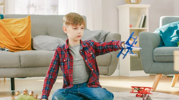 Em casa: Rapaz esperto brinca com avião de brinquedo. Criança brincando em um tapete na sala de estar ensolarada . — Fotografia de Stock