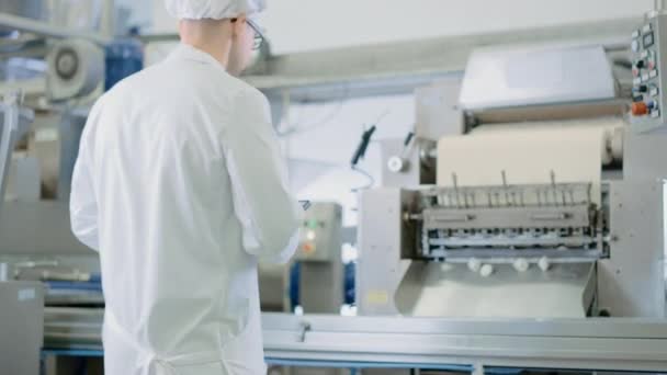 Young Male Quality Supervisor or Food Technician is Inspecting the Automated Production at a Dumpling Food Factory. Employee Uses a Tablet Computer for Work. He Wears a White Sanitary Hat and Work Robe. — Stock Video