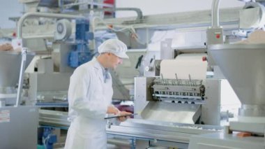 Genç Erkek Kalite Danışmanı veya Gıda Teknisyeni Bir Köfte Gıda Fabrikasında Otomatik Üretim Teftiş olduğunu. Çalışan İş İçin Tablet Bilgisayar Kullanıyor. Kameraya Bakıyor ve Gülümsüyor.