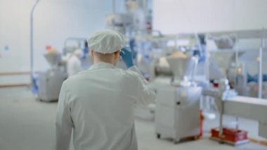 Bir Köfte Fabrikasında Genç Erkek Gıda Çalışanı Konveyör Bant geliyor. İş Arkadaşıyla Birlikte Çalışmaya Başlar ve Dash'teki Ayarları Ayarlar. Beyaz Hijyenik Şapka ve Lateks Eldiven Giyerler.