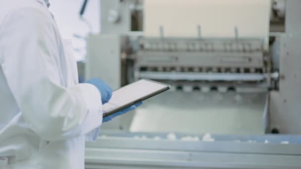 Le jeune superviseur de la qualité ou technicien alimentaire inspecte la production automatisée dans une usine alimentaire. CLose Up Plan d'un employé utilisant un ordinateur tablette pour le travail. Il tape dans les données tout en portant des gants en latex . — Video