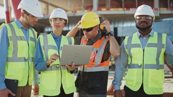 Une équipe diversifiée de spécialistes utilise un ordinateur portable sur le chantier de construction. Projet de construction immobilière avec des machines : Ingénieur civil, investisseur, femme d'affaires et constructeur discutant du plan directeur — Video