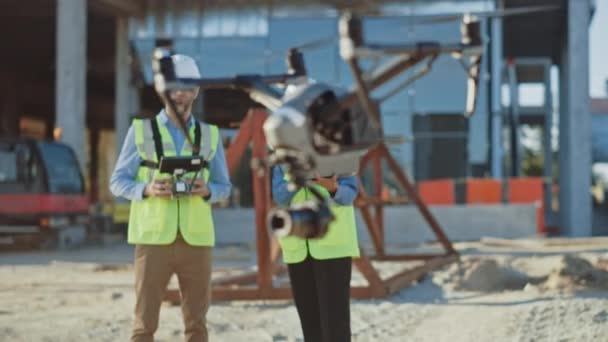 Dois especialistas controlando drone no canteiro de obras. Engenheiro Arquitetônico e inspetor de engenharia de segurança voam drone na construção civil local de controle de qualidade. Concentre-se em Drone — Vídeo de Stock