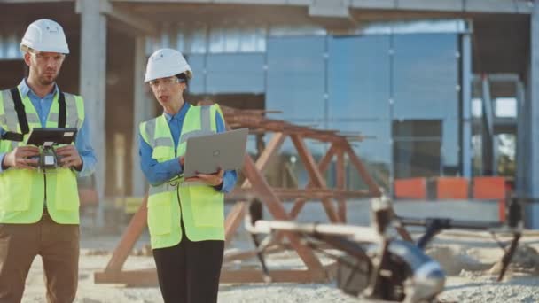 Két specialista irányítja a drónt egy építkezésen. Építészeti Mérnök és Biztonsági Mérnök Felügyelő Fly Drone on Commercial Building Construction Site Controlling Design and Quality — Stock videók