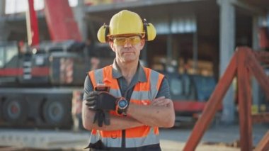 Başarılı Builder Portresi / İşçi / Yüklenici Bir Ticari Yapı Şantiye ayakta Sabit Şapka ve Güvenlik Yelek Giyen, Güvenle Silah Haçlar. Arka Plan Vinç Makinaları