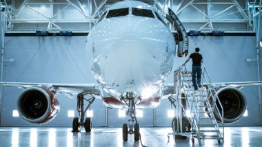 Brand New Airplane Standing in a Aircraft Maintenance Hangar while Aircraft Maintenance Engineer/ Technician/ Mechanic goes inside Cabin via Ladder/ Ramp. clipart