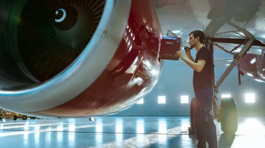 Bir Hangar uçak bakım genç mühendisi olarak / teknisyen / mekanik Tablet bilgisayar ile uçak Jet motoru inceler. O motor kapağı açar ve bir el feneri ile iç inceliyor.