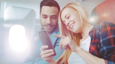 Ticari uçak bir gemide güzel genç sarışın yakışıklı İspanyol erkek ile kullanma Smartphone ve gülmek. Uçak pencereden güneş parlıyor.