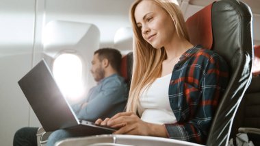On Board of Commercial Airplane Beautiful Young Blonde Works on a Laptop while Her Hispanic Male Neighbor Sleeps. clipart