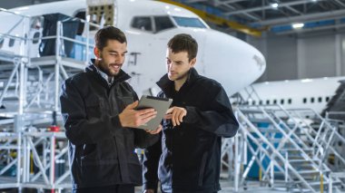 Uçak bakım işçi ve mühendis konuşmayı. Tablet holding.