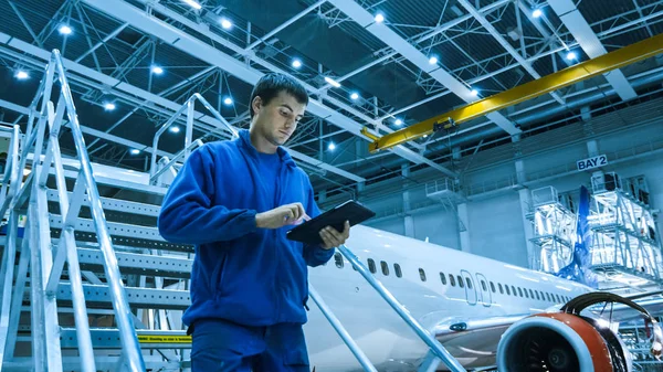 Mecânico de manutenção de aeronaves em uniforme azul está descendo as escadas enquanto usa tablet em um hangar . — Fotografia de Stock