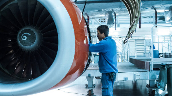 Aircraft maintenance mechanic inspects and tunes plane engine in a hangar.
