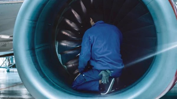 Mecánico de mantenimiento de aeronaves con luz de destello inspecciona palas de turbina planas en un hangar . — Foto de Stock