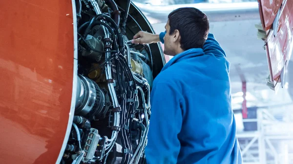 Mecânico de manutenção de aeronaves inspeciona e sintoniza o motor de avião em um hangar . — Fotografia de Stock