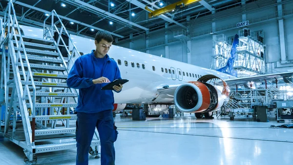 Mecánico de mantenimiento de aeronaves en uniforme azul está bajando las escaleras mientras usa la tableta en un hangar . — Foto de Stock