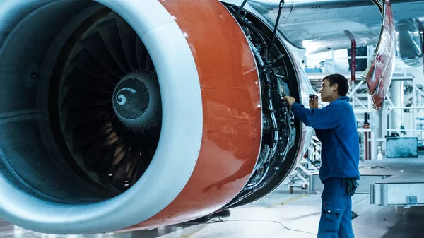 Flygmekaniker underhåll med en blixt ljus inspekterar plan motor i en hangar. — Stockfoto