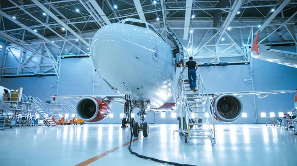 Новый самолет, стоящий в ангаре технического обслуживания самолетов, в то время как инженер по техническому обслуживанию самолетов / техник / механик входит в кабину через лестницу / рампу . — стоковое фото