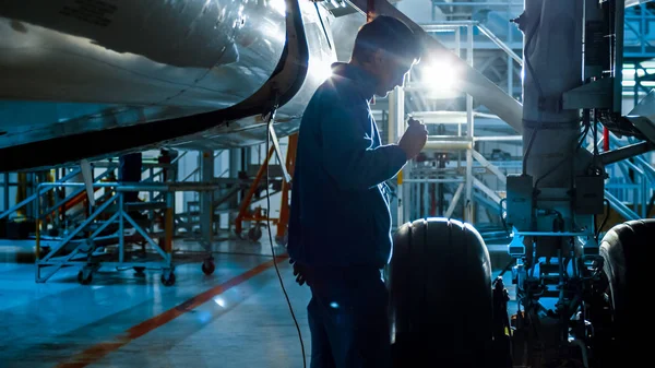 Un mécanicien d'entretien d'aéronef muni d'un flash inspecte un châssis d'avion dans un hangar . — Photo