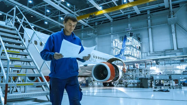 Underhåll flygmekaniker i blå uniform kommer ner för trappan medan du läser tidningar i en hangar. — Stockfoto