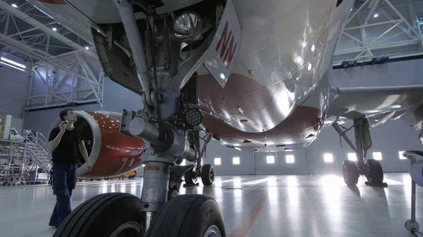 En un hangar Ingeniero / Técnico / Mecánico de Mantenimiento de Aeronaves inspecciona visualmente el chasis y el cuerpo / fuselaje del avión que camina debajo de él . —  Fotos de Stock