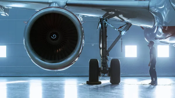 In a Hangar Aircraft Maintenance Engineer / Technician / Mechanic Visually Inspects Airplane 's Jet Engine . — стоковое фото