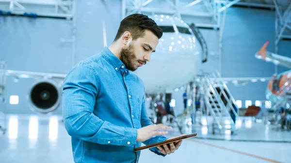 Im großen Firmenhangar Flugzeugwartungsingenieur nutzt Tablet-Computer, während er in der Nähe eines großen neuen, glänzend weißen Flugzeugs steht. — Stockfoto