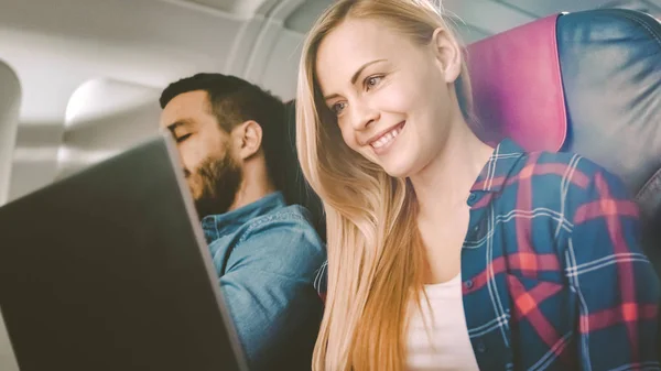 Na pokładzie z komercyjnego samolotu piękna Młoda Blondynka działa na laptopie podczas jej Hiszpanie mężczyzna sąsiada śpi. — Zdjęcie stockowe