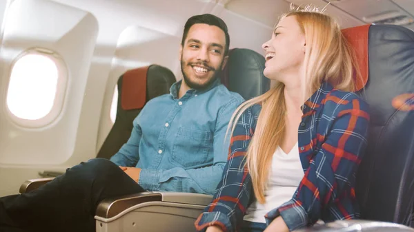 Kaupallisella lentokoneella Komea latinomies kertoo hauska tarina hänen kaunis blondi tyttöystävä. Molemmat nauravat. He matkustavat New Airplane, Sun paistaa ikkunan läpi . — kuvapankkivalokuva
