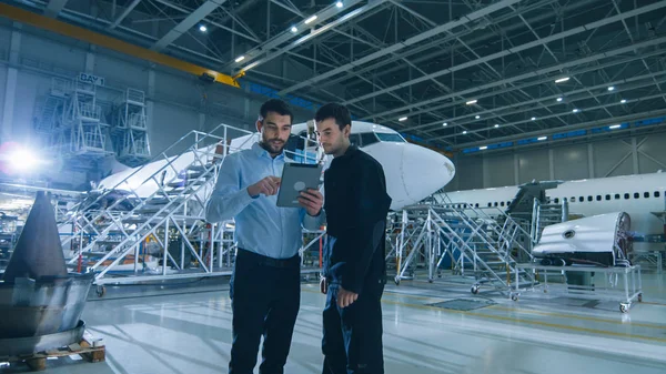 Aircraft Maintenance Worker and Engineer having Conversation. Holding Tablet.