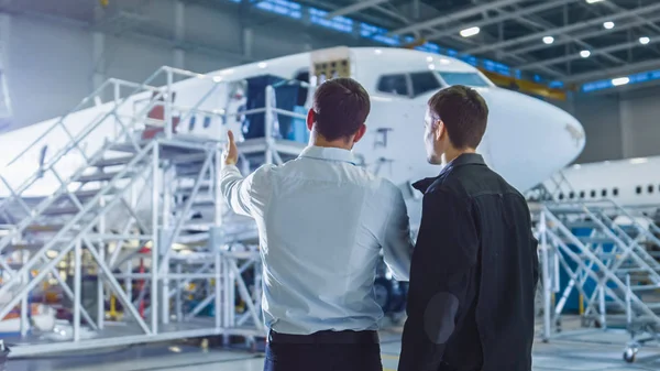 Trabalhador e Engenheiro de Manutenção de Aeronaves Conversando. Olhando para o avião . — Fotografia de Stock