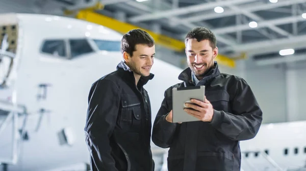 Aircraft Maintenance Workers having Conversation. Holding and using Tablet.