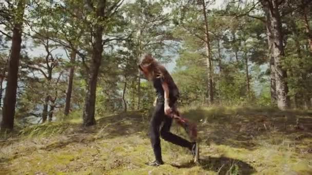 Happy Beautiful młoda kobieta spacery i tańce w europejskim lesie sosnowym. To ciepły słoneczny dzień w przyrodzie. Ona uśmiecha się i twistów w słońcu. lasy są zielone i dzikie. Dziewczyna jest ubrana w czarny. — Wideo stockowe