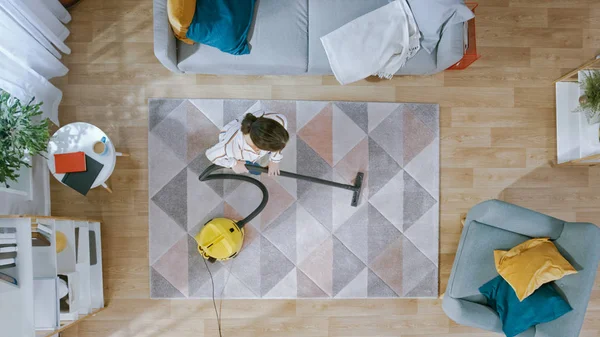 Timelapse of Young Female Limpando uma sala de estar acolhedora com um aspirador de pó. Interior moderno com tapete, sofá, cadeira, mesa de café, prateleira, planta e piso de madeira. Vista superior . — Fotografia de Stock