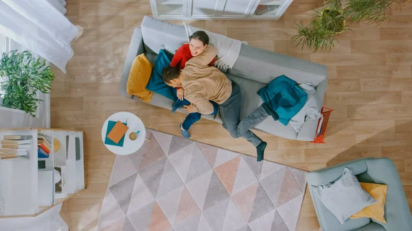 Jeune beau couple est amusant et faire la fête autour. Courir à travers la pièce et s'allonger sur le canapé. Salon confortable avec intérieur moderne avec des plantes, une table et du parquet. Vue du dessus . — Photo