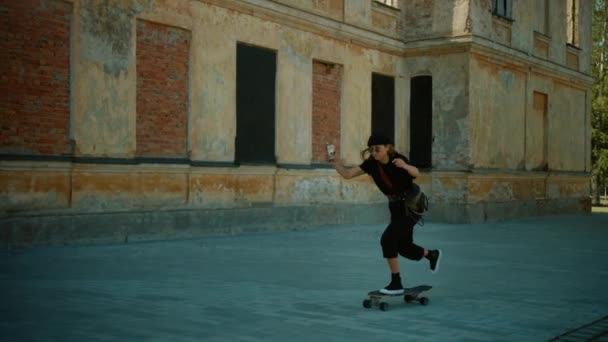 Fresco ragazza che indossa berretto e occhiali da sole rotondi equitazione Skateboard attraverso elegante fianchi parte della città. Skateboard nel distretto di Hipster. rallentatore dopo colpo — Video Stock