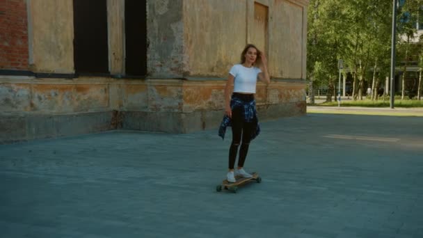 Linda menina loira cavalgando em um Longboard através Hipster District. Elegante Teenager Skateboarding na parte legal da cidade. Movendo câmera lenta movimento tiro — Vídeo de Stock