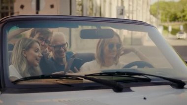 İki Güzel Kız ve İki Şık Guys Chilling ve Cabrio Arabada Eğlenmek, Akıllı Telefonlar kullanarak, Sosyal Medya gönderme. Seyahat Eden, Konuşan Gençler
