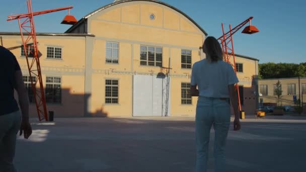 Grupp av skaters, två vackra flickor och en snygg pojke rida på skateboards och longboards. I bakgrunden post industriella lager och snygg hipster District — Stockvideo