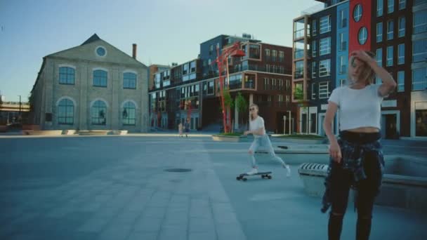 Två vackra tonårsflickor och en stilig kille rida på skateboards genom fashionabla hipster distrikt. Vackra unga människor Skateboarding genom modern snygg stadsgata. Efter slow motion kamera skott — Stockvideo