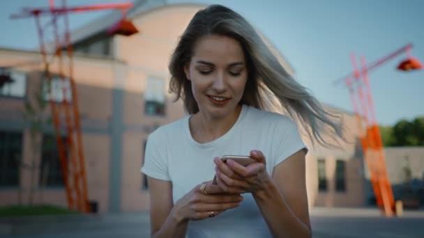 Linda menina patinadora loira vestindo roupas casuais, usa Smartphone, compartilhando coisas nas mídias sociais, tirando selfies, mensagens de amigos e se divertindo enquanto está sentado em um banco em Hipster na moda — Vídeo de Stock