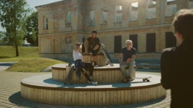 Şık Cool Gençler Park Banklar üzerinde Chilling. İki Kız ve İki Erkek Onların Kaykaylar ile Dinlenme, Konuşma ve Eğlenmek. Şık Post Sanayi Parkı Şehrin Gentrified Bölümünde